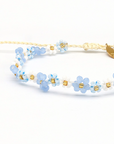 A delicate beaded necklace with light blue and white flower beads, separated by small gold spacer beads, on a white background.
