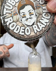 Person holding a bottle of 'Tubby Tom's Rodeo Ranch' butter with a decorative label.