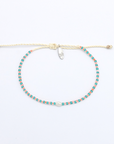 A delicate beaded bracelet with turquoise and pink beads on a cream-colored cord, featuring a small silver-toned crystal charm, displayed on a clean white background.