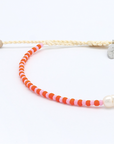 A beaded bracelet featuring alternating bright orange and light pink beads, accented by a single white pearl bead and a small silver-toned oval charm, on a white background.