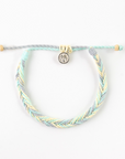 A braided cord bracelet in pastel mint green, light blue, and pale yellow, featuring a small silver-toned circular charm with a palm tree design, displayed on a clean white background.
