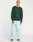 Man wearing a green sweater and light blue jeans on a white background