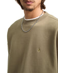 Man wearing a green sweater with a small logo and a chain necklace on a white background