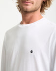 Man wearing a white long-sleeve shirt with a small logo on a plain background