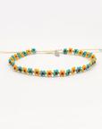 A beaded stretch bracelet featuring small daisy-like flowers in turquoise, yellow, and orange with a tiny silver heart charm, displayed on a clean white background.