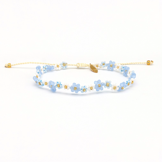 A delicate beaded bracelet featuring light blue and white flower beads with gold accents, including a small gold leaf charm, on a white background.