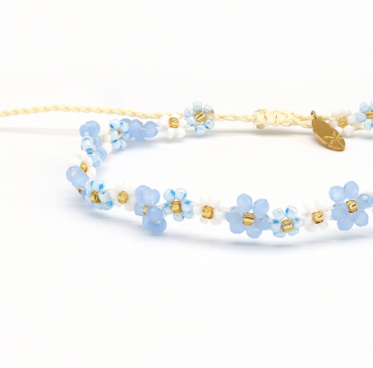 A delicate beaded necklace with light blue and white flower beads, separated by small gold spacer beads, on a white background.