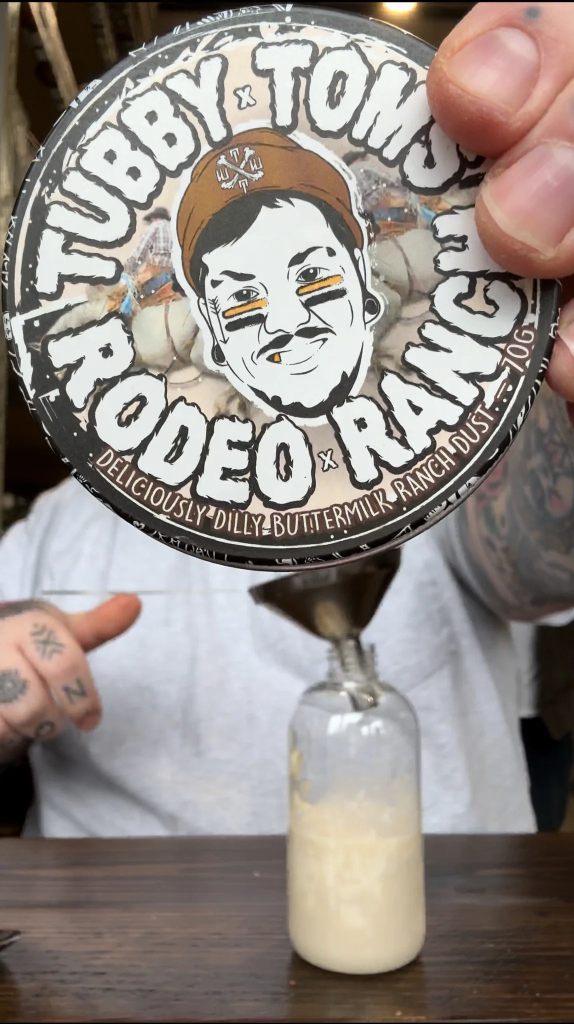 Person holding a bottle of 'Tubby Tom's Rodeo Ranch' butter with a decorative label.