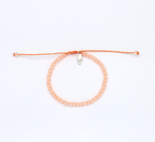 A peach-colored beaded bracelet with a matching adjustable orange cord and a small silver-toned metal charm, displayed on a clean white background.