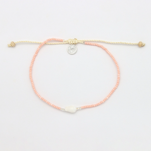 A delicate beaded bracelet with peach-pink round beads, a cream-colored adjustable cord, a small silver circular charm, and a white central bead, displayed on a clean white background.