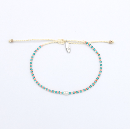 A delicate beaded bracelet with turquoise and pink beads on a cream-colored cord, featuring a small silver-toned crystal charm, displayed on a clean white background.