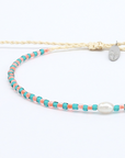A delicate double-strand necklace featuring a cream-colored braided cord with a small silver pendant, alongside a beaded strand of turquoise and coral beads with a white pearl accent, displayed on a clean white background.