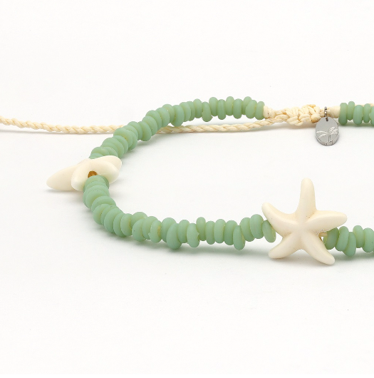A beaded necklace with light green round beads, a cream braided cord, a white starfish charm, and a small silver star-shaped charm on a white background.
