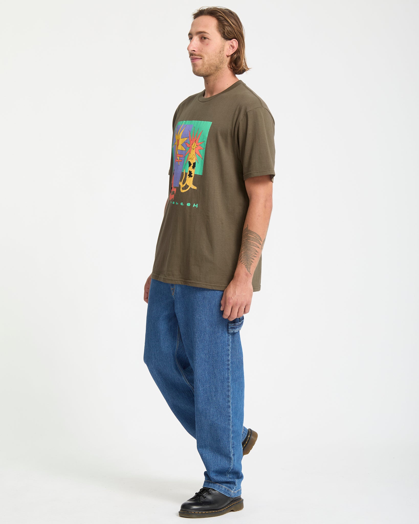 Man wearing a green t-shirt with a colorful graphic and blue jeans on a white background