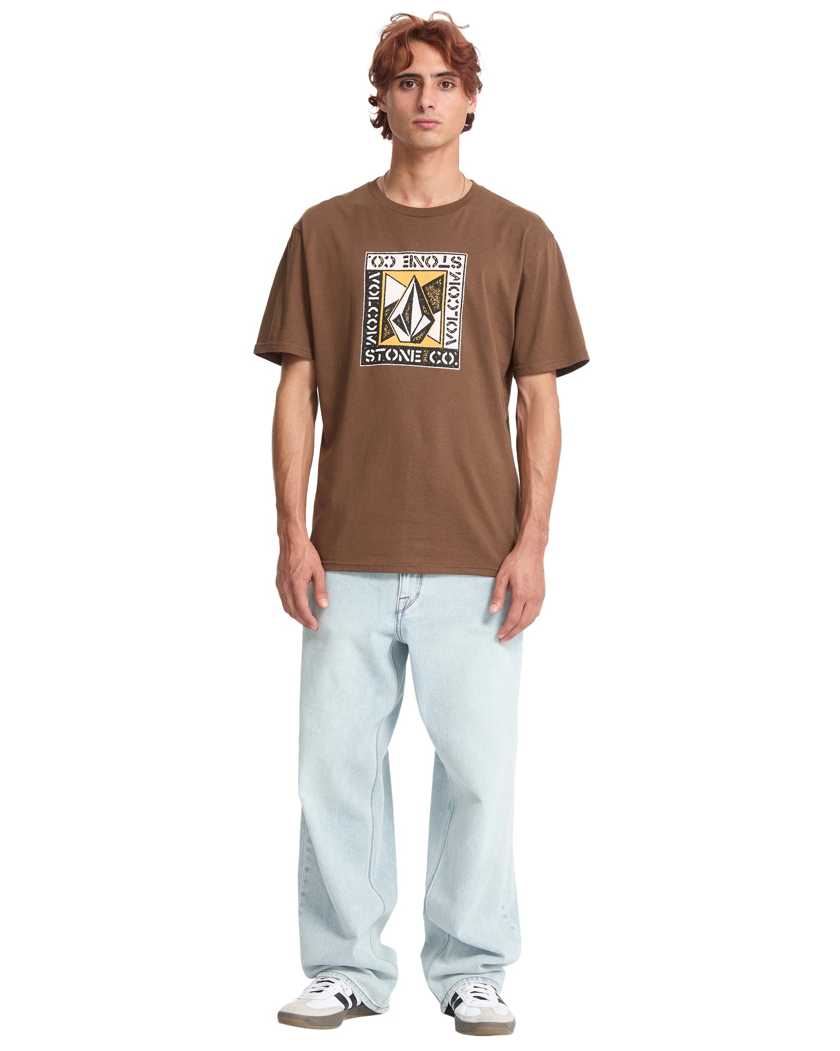 Person wearing a brown t-shirt with a logo and text, standing against a white background