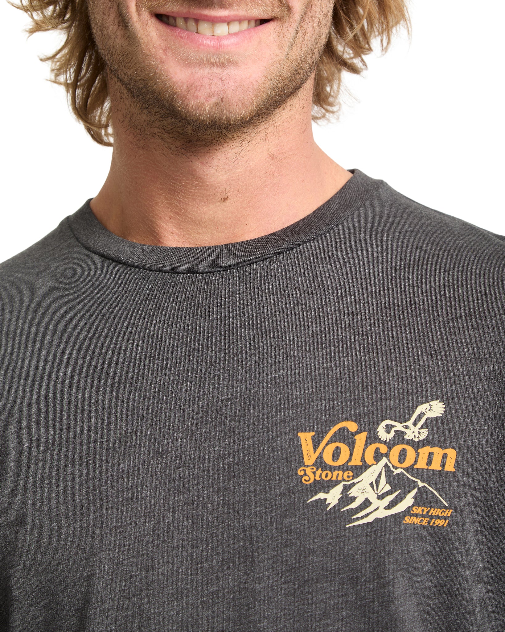 Man wearing a dark gray Volcom t-shirt with a logo on a white background