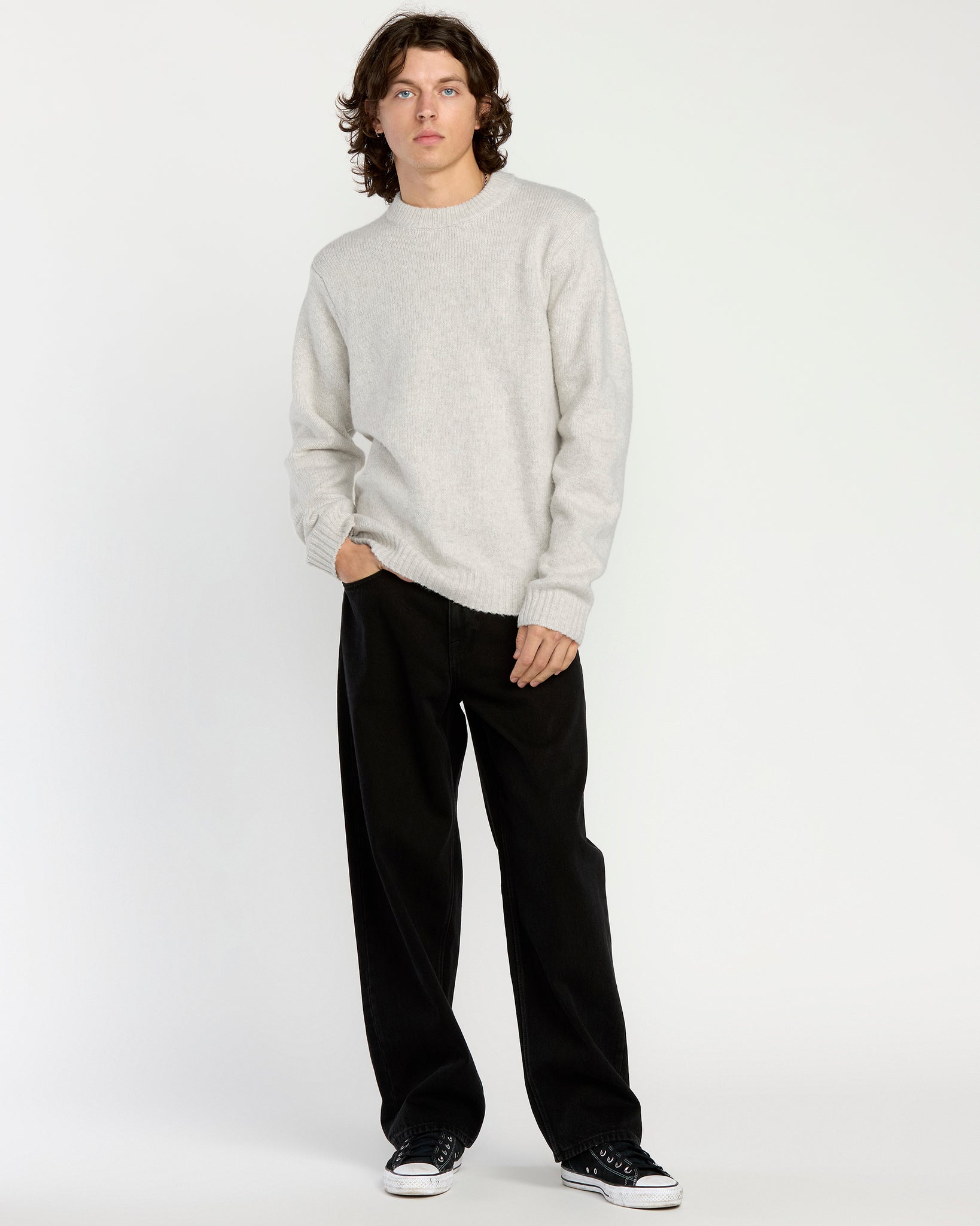 Man wearing a light gray sweater and black pants on a white background