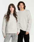 Two people wearing light gray sweaters and dark pants against a white background