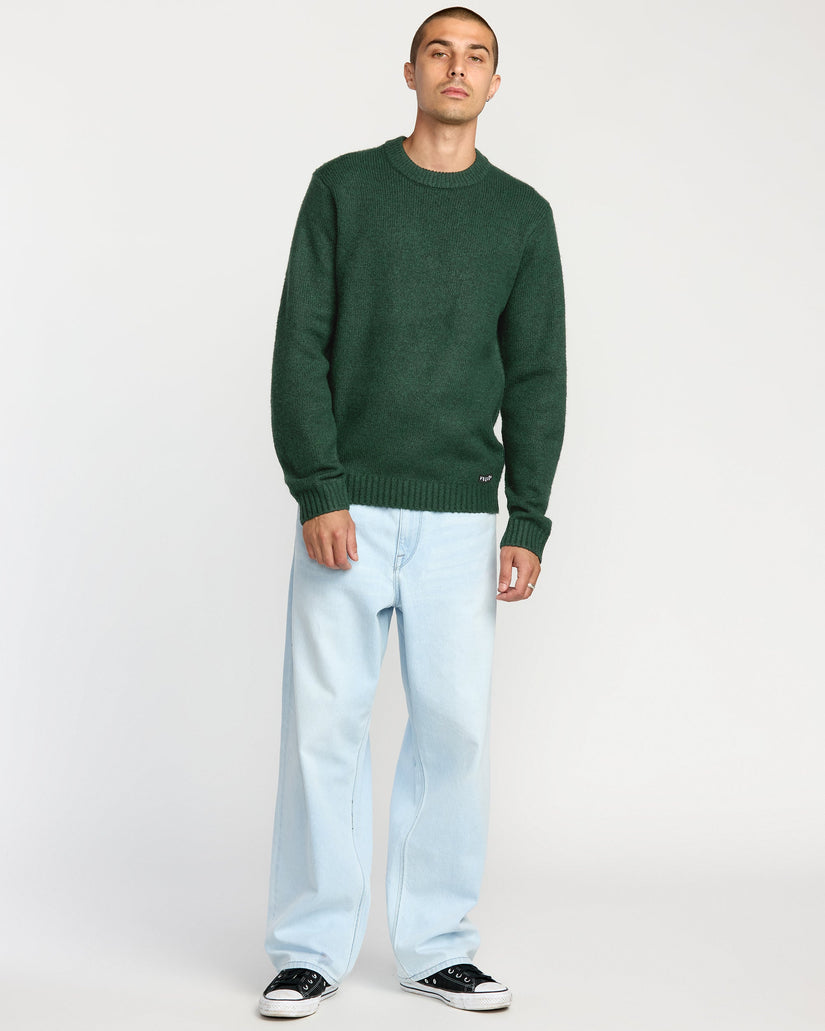 Man wearing a green sweater and light blue jeans on a white background