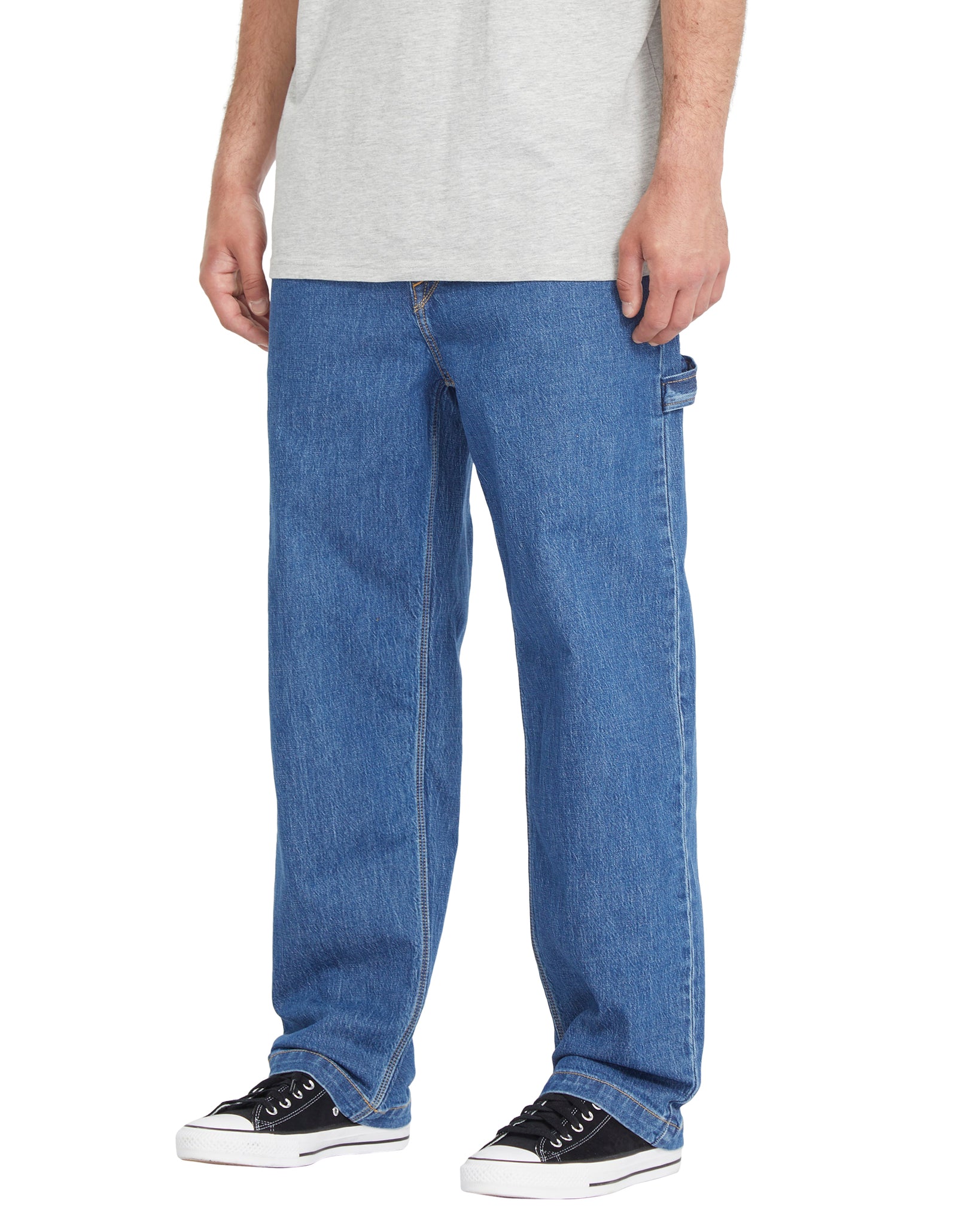 Person wearing blue jeans and black sneakers on a white background