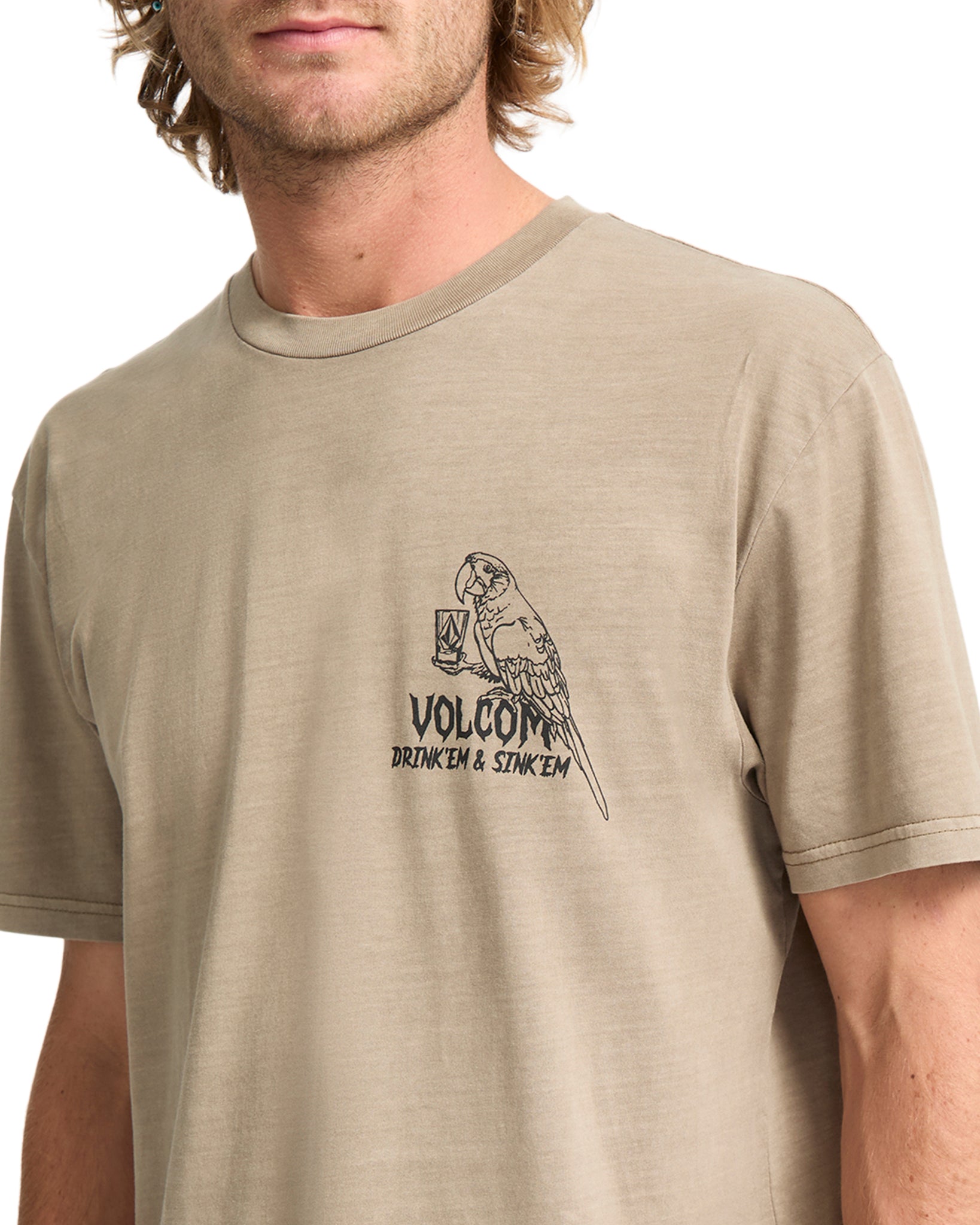 Man wearing a beige Volcom t-shirt with a logo on a white background