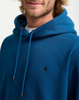 Person wearing a blue hoodie with a small logo on a white background