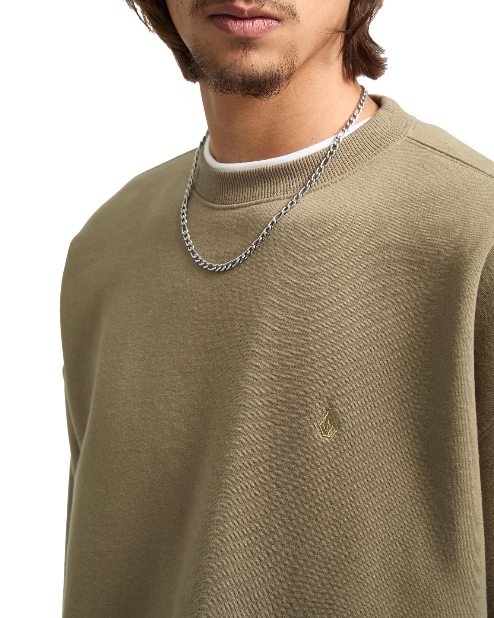 Man wearing a green sweater with a small logo and a chain necklace on a white background
