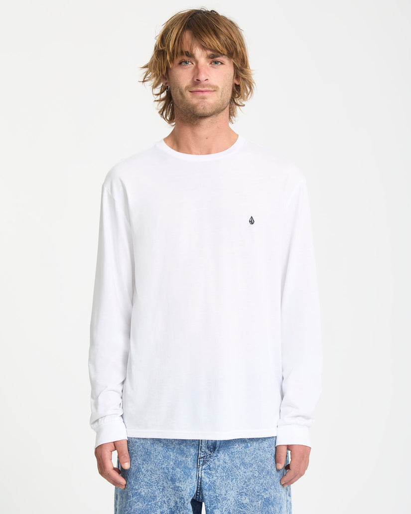 Man wearing a white long-sleeve shirt with a small logo on a plain background