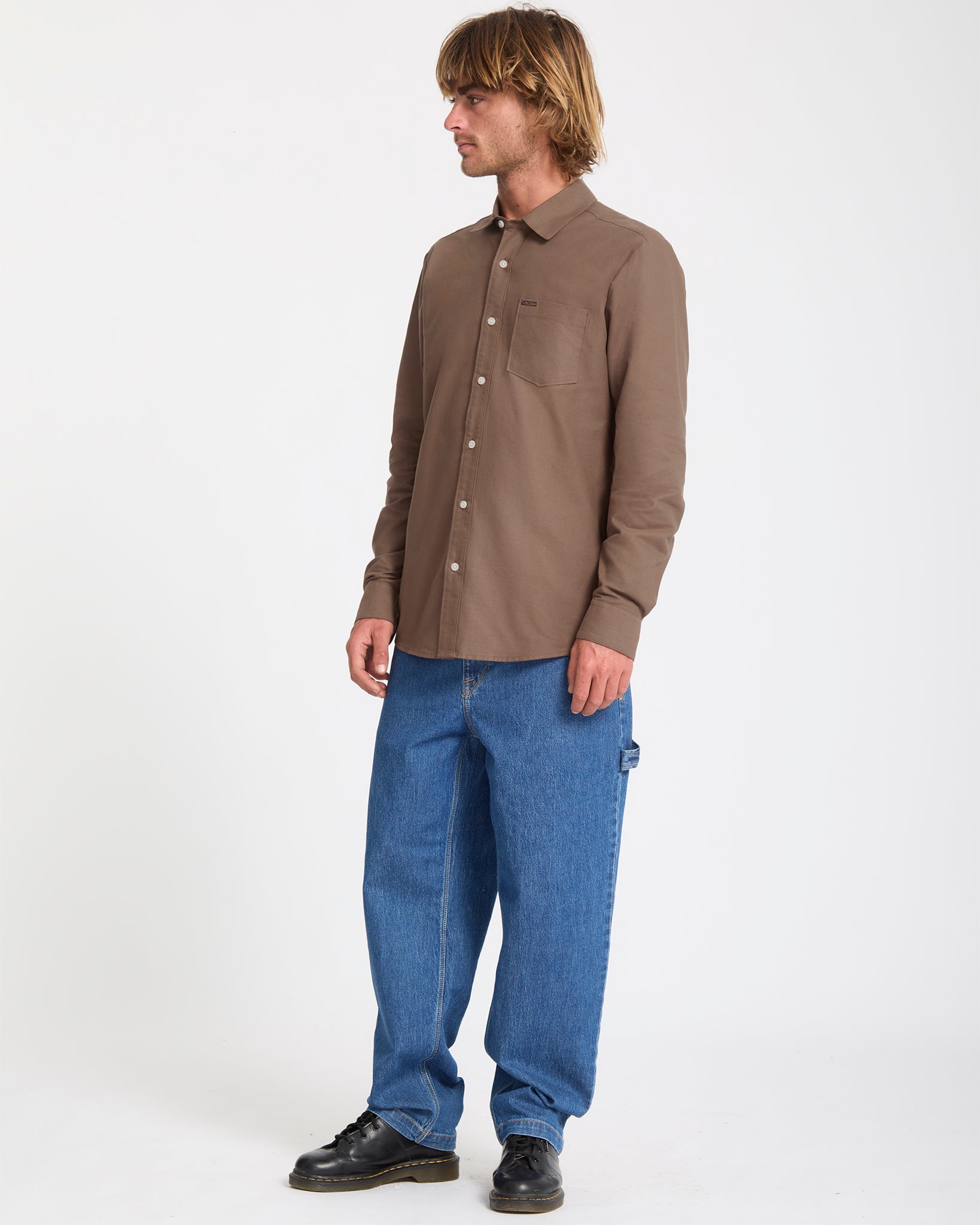 Man wearing a brown shirt and blue jeans on a white background