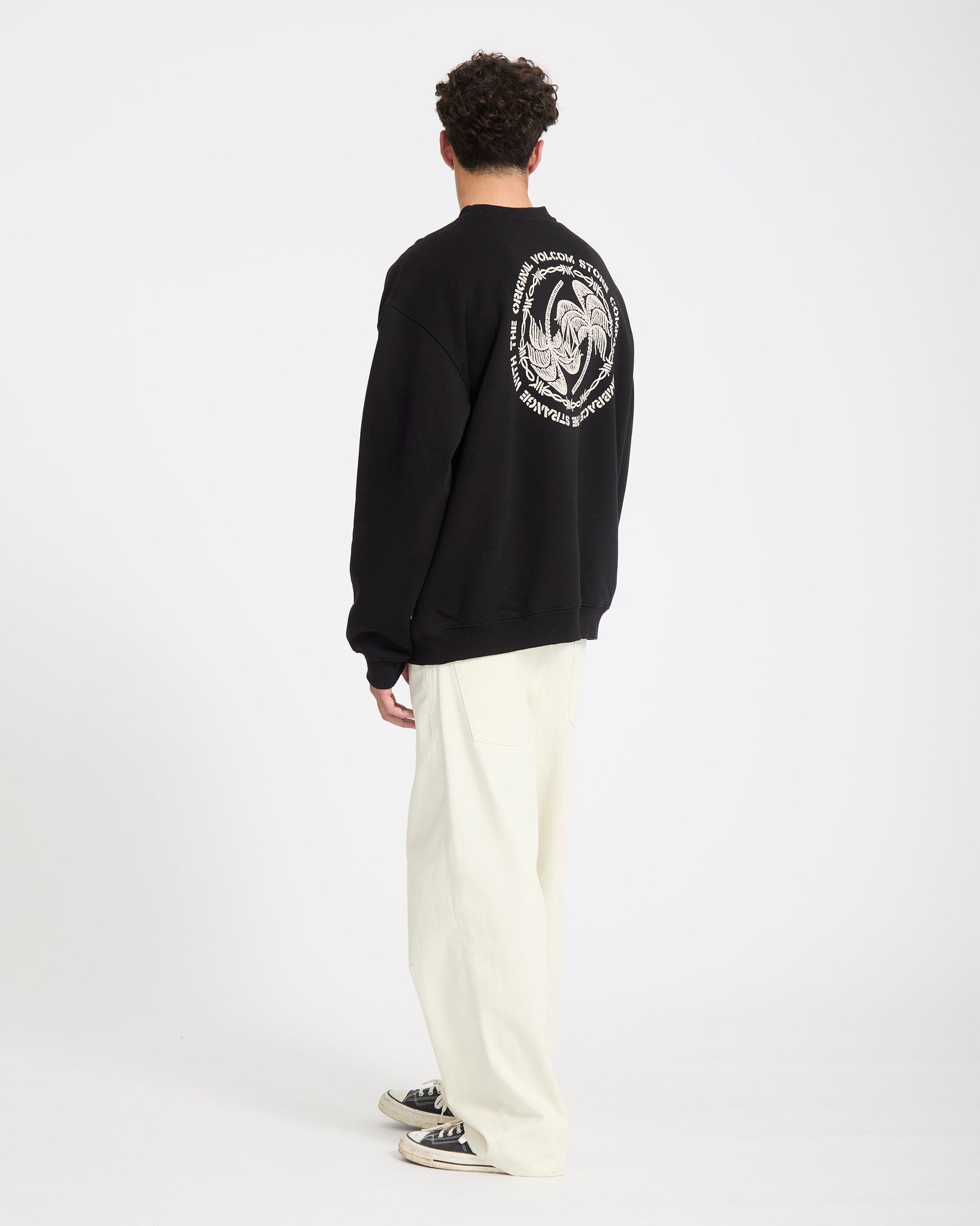 Person wearing a black Volcom sweatshirt with a white logo on the back, standing against a white background