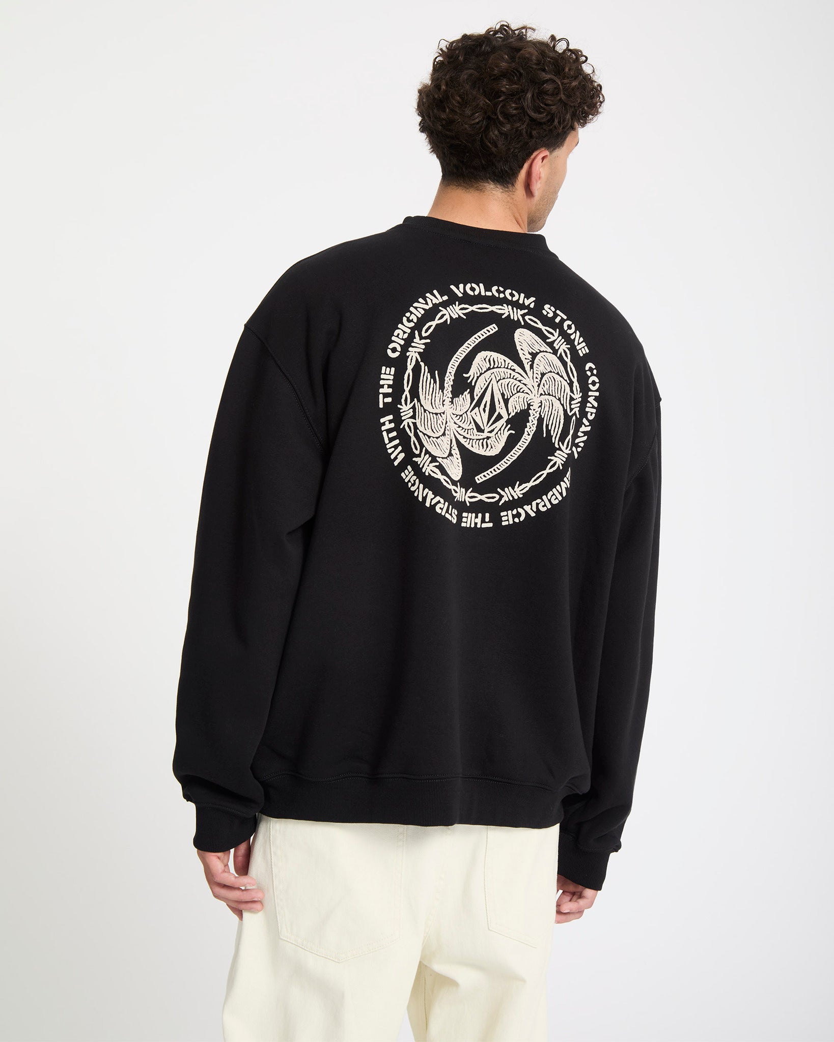Person wearing a black sweatshirt with a white Volcom logo on the back against a white background