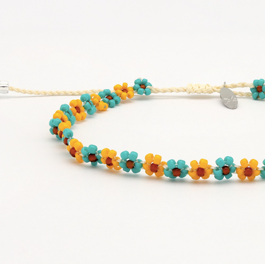A beaded necklace featuring alternating yellow and turquoise flower beads with small orange centers, strung on a cream-colored cord with a silver heart-shaped clasp.