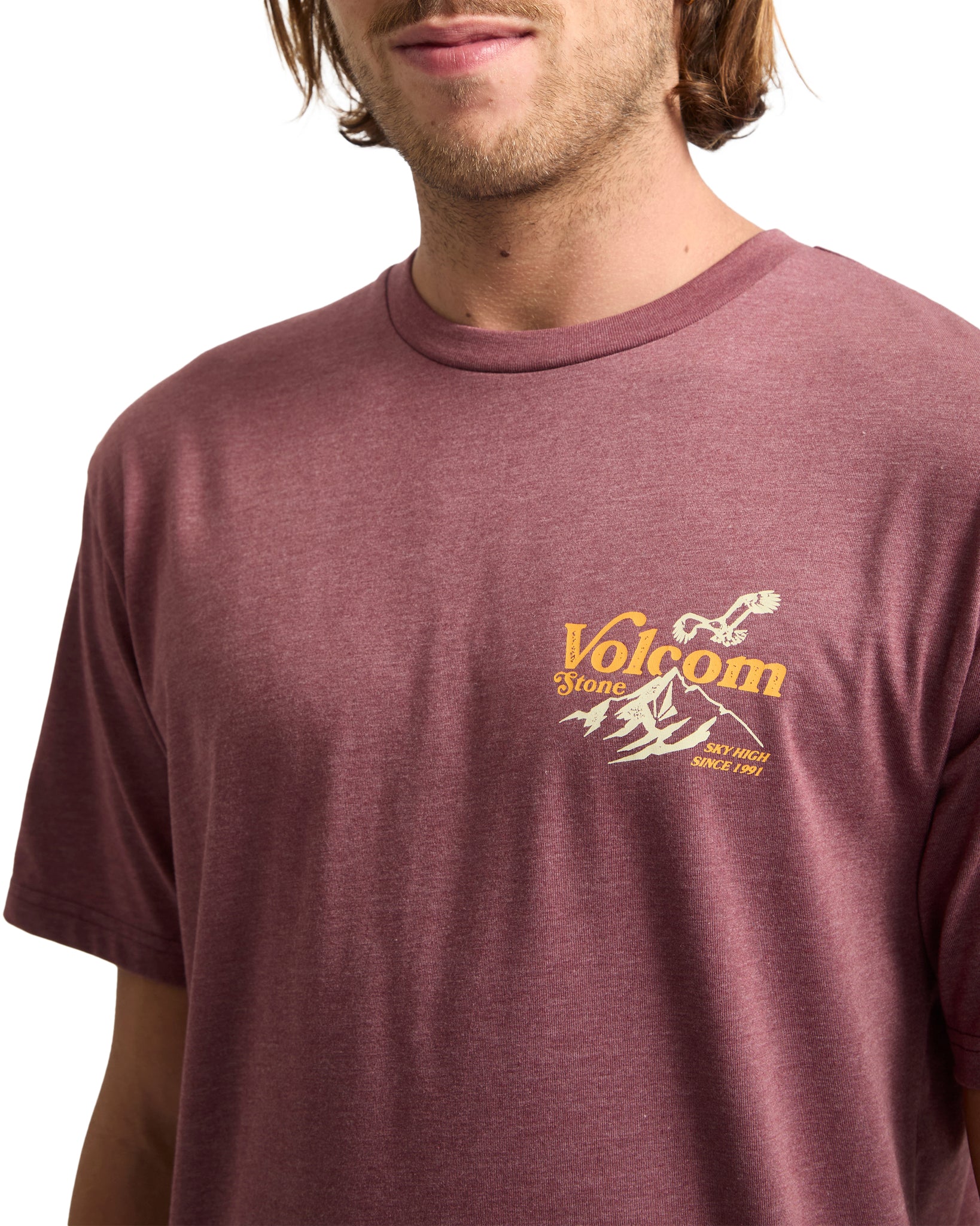 Man wearing a maroon Volcom t-shirt with a logo on a white background